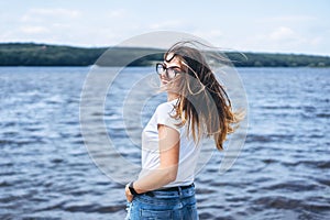 Portrait of a beautiful young woman in stylish glasses. Girl in white tshirt posing on the background of the lake landscape