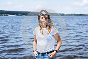 Portrait of a beautiful young woman in stylish glasses. Girl in white tshirt posing on the background of the lake landscape