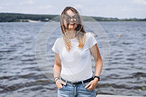 Portrait of a beautiful young woman in stylish glasses. Girl in white tshirt posing on the background of the lake landscape