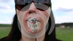 Portrait of a beautiful young woman on a summer lawn blowing on a ripe dandelion on a sunny day outdoors. Enjoy nature. Allergy fr