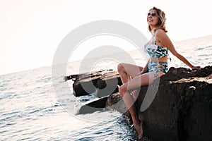 Portrait of beautiful young woman in sunglasses and bikini on beach. Female model posing in swimsuit on sea shore