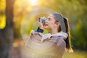 Portrait of beautiful young woman taking photos with vintage camera outdoors in the nature