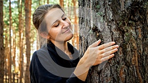 Portrait of beautiful young woman touching and looking big old tree at forest. Concept of ecology, environment