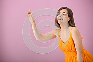 Portrait of beautiful young woman touching something on color background