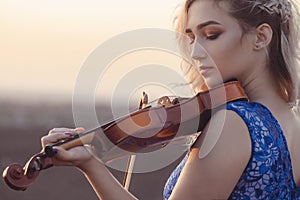 Portrait of a beautiful young woman with a violin under her chin at sunset, girl playing a musical instrument on nature, concept