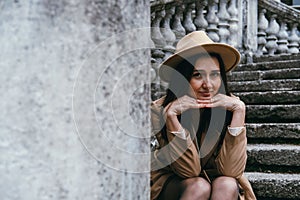 Portrait of beautiful young woman wearing beige hat and coat, sitting on stairs