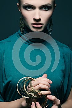 Portrait of a beautiful young woman wearing green blue dress and ethnic earrings, bracelets. Model posing over light-blue