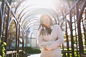 Portrait of beautiful young woman wearing light casual clothes. Girl standing under sunshine archway with headphones on