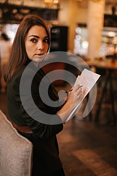 Portrait of beautiful young woman wearing stylish clothes in restaurant holding paper documents.