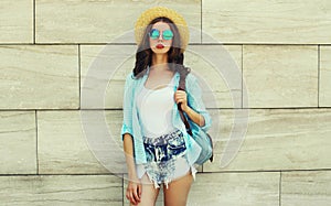 Portrait beautiful young woman wearing a summer straw hat, shorts and backpack in the city on an urban background
