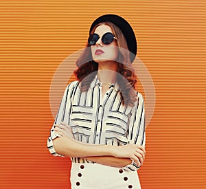 Portrait beautiful young woman wearing a white striped shirt, black round hat on orange background
