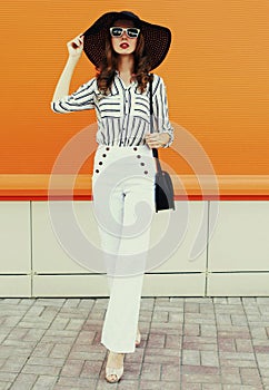 Portrait beautiful young woman wearing a white striped shirt, black round hat on orange background