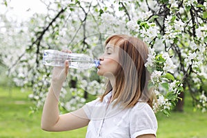 Portrait of a beautiful young woman who drinks water in park among blossoming trees