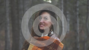 portrait of a beautiful young woman who smiles and in a warm blanket against the backdrop of the autumn forest slow