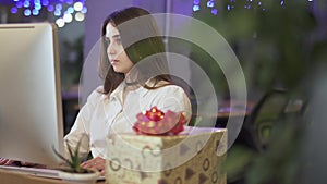 Portrait of beautiful young woman working by the computer near beautiful present box on the background of modern office