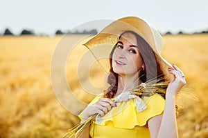 Portrait of a beautiful young woman in a yellow dress with a straw hat on a Golden wheat field at sunset. Sensual girl is enjoying