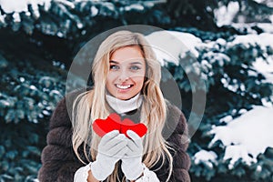 Portrait of a beautifull smiling woman in the forest holding red Valentine`s heart in the hands. Valentine`s Day