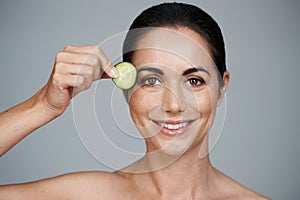 Portrait, beauty and cucumber with smile of woman in studio on gray background for natural wellness. Face, antiaging or