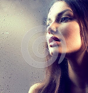 Portrait of beauty girl behind the wet glass