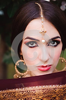 Portrait of beauty Indian model with bright make-up who hiding her face behind the veil. Young Hindu woman with mehndi