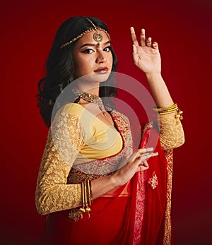Portrait, beauty and Indian woman with fashion, traditional dress and luxury against a red studio background. Face