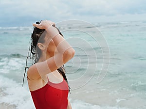 Portrait of a beauty woman on the beach with beautiful tanned skin and wet hair in a red swimsuit against the ocean
