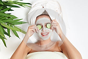 Portrait of beauty woman laying with towel on the head, cucumber on her eyes, facial mask. Spa therapy. Relax.