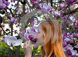 Portrait of beauty young redhead woman smelling to magnolia tree, side view with closed eye