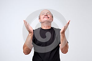 Portrait of begging caucasian man in casual outfit, holding hands in pray and looking up hopefully, praying