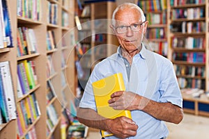 Portrait of bespectacled intelligent older man in library with book in hands