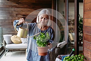 Portrait of beutiful mature woman taking care of plants on balcony. Spending free weekend at home.