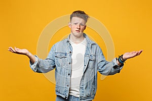 Portrait of bewildered upset young man in denim casual clothes pointing spreading hands aside isolated on yellow orange