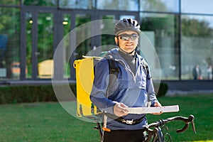 Portrait of bicycle courier with yellow bag and bike. Man in helmet and glasses holding pizza box