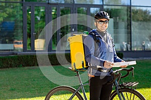 Portrait of bicycle courier with yellow bag and bike. Man in helmet and glasses holding pizza box