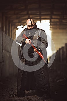 Portrait of big brutal man with rifle in leather coat as Mad Max style at abandoned building