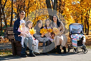 Portrait of big family with children in an autumn city park, happy people sitting together on a wooden bench, posing and smiling,