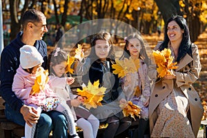 portrait of big family with children in an autumn city park, happy people sitting together on a wooden bench, posing and smiling,