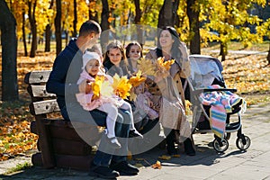 portrait of big family with children in an autumn city park, happy people sitting together on a wooden bench, posing and smiling,