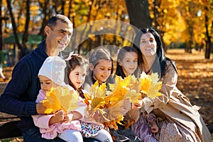 portrait of big family with children in an autumn city park, happy people sitting together on a wooden bench, posing and smiling,