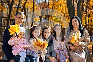 portrait of big family with children in an autumn city park, happy people sitting together on a wooden bench, posing and smiling,