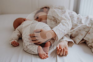 Portrait of big sister cuddling newborn, little baby. Girl lying with her new sibling in bed, closed eyes. Sisterly love