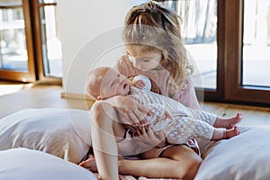 Portrait of big sister holding newborn sister. Girl carefully cuddling small baby. Sisterly love, joy for new family