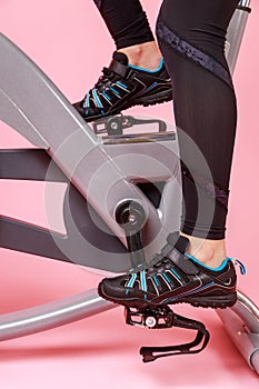 Portrait of the bike simulator and women's legs in black sneakers, cardio workout, training.