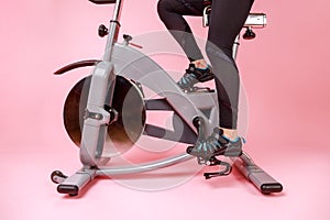 Portrait of the bike simulator and women& x27;s legs in black sneakers and leggins, cardio workout.