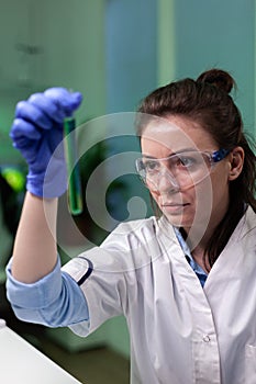 Portrait of biochemist doctor looking at medical test tube with green dna solution