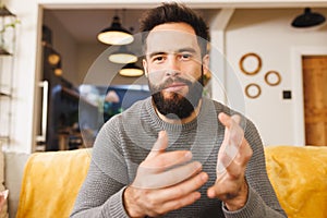 Portrait of biracial bearded smiling young man gesturing while sitting on sofa in living room