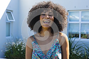 Portrait of biracial beautiful mid adult woman with afro hair laughing against house in yard