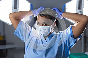 Portrait of biracial female surgeon wearing scrubs and face mask in operating theatre