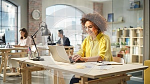 Portrait of Biracial Young Woman Using Laptop and Smiling in a Spacious Office. Female Technical