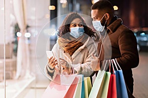 Portrait of black couple using phone wearing masks near mall